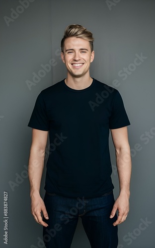 A man wearing a black t-shirt and jeans, standing in front of a gray background with a slight smile on his face, t-shirt mockup.