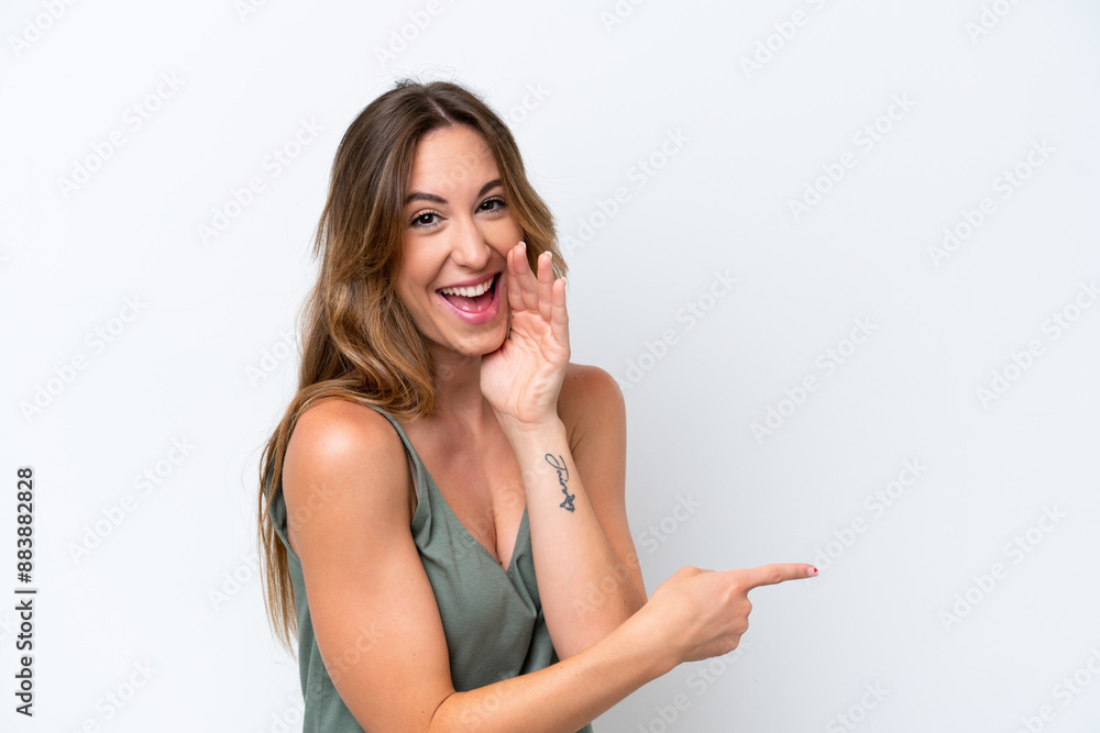 Young caucasian woman isolated on white background pointing to the side to present a product and whispering something Young caucasian woman isolated on white background pointing to the side to present a product and whispering something