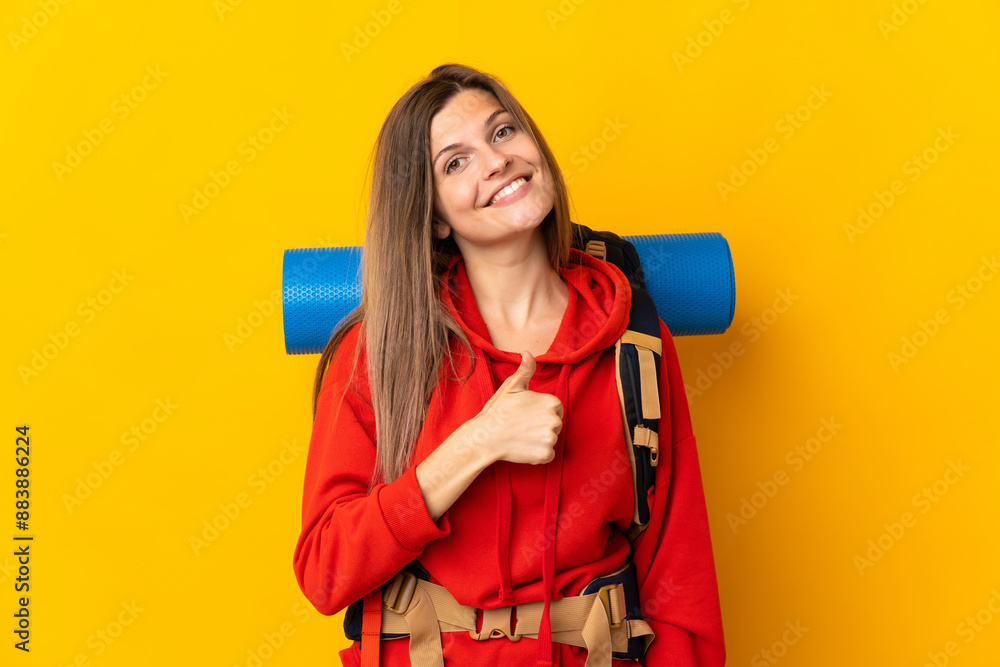Slovak mountaineer woman with a big backpack isolated on yellow background giving a thumbs up gesture Slovak mountaineer woman with a big backpack isolated on yellow background giving a thumbs up gesture
