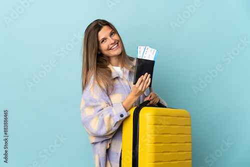 Young Slovak woman isolated on blue background in vacation with suitcase and passport photo