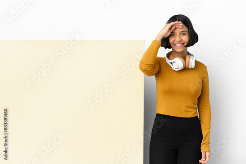 Young woman listening music with a big empty placard over isolated background saluting with hand with happy expression photo