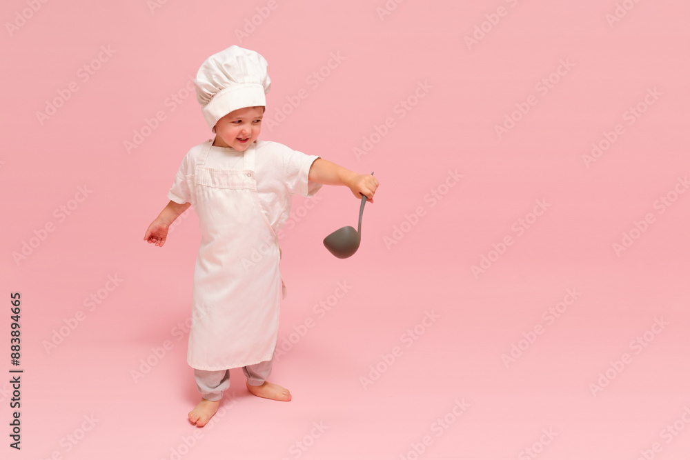A young child in a chef's outfit holding a ladle. Studio portrait on pink background. Kid aged 3 years (three year old boy) A young child in a chef's outfit holding a ladle. Studio portrait on pink background. Kid aged 3 years (three year old boy)