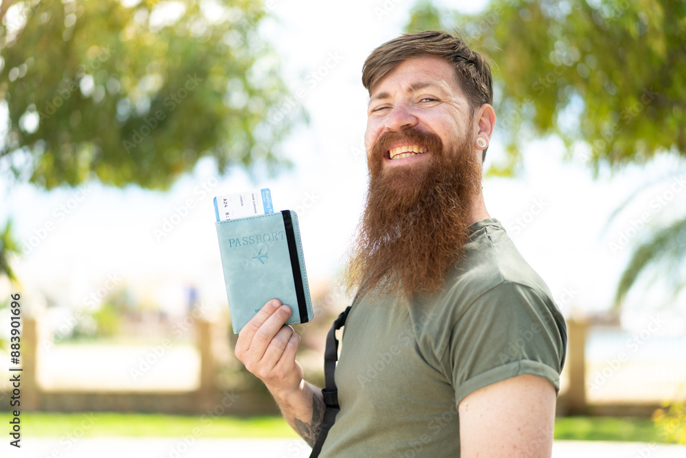 Fototapeta premium Redhead man with beard holding a passport at outdoors smiling a lot