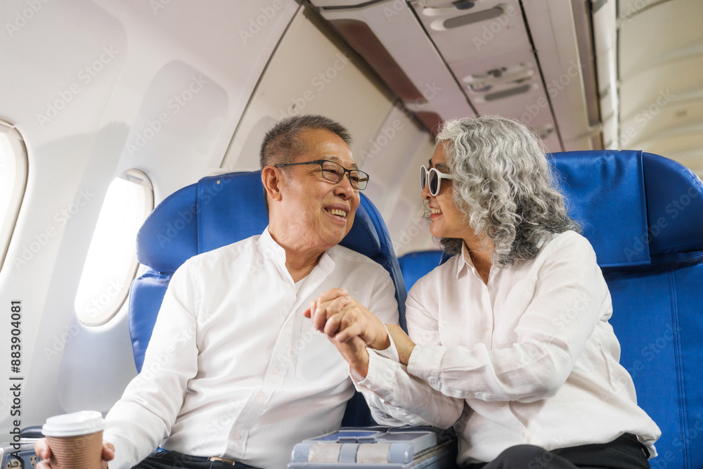 Obraz premium A mature couple enjoys a plane ride sitting near the window. They looked out into the sky. Immerse yourself in the scenery and excitement of the journey. To create precious memories together