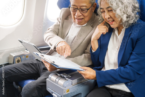 A mature couple enjoys a plane ride, seated near the window. They gaze out at the sky, savoring the view and the excitement of travel, creating cherished memories together.