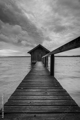 Atmospheric view over a jetty to a boathouse on Lake Ammersee in Bavaria, Germany, on a cloudy day.