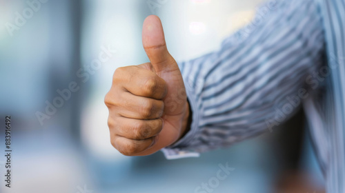 Close-up of a hand giving a thumbs-up gesture, representing approval or success, against a blurred background. Perfect for business or motivational themes.