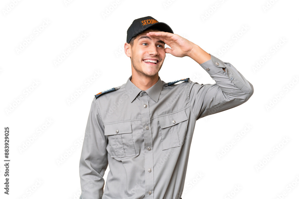 Young security man over isolated background looking far away with hand to look something Young security man over isolated background looking far away with hand to look something