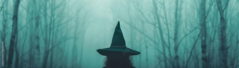 Fototapeta premium A mysterious figure in a witch's hat stands in a foggy forest, invoking a sense of magic and dark fantasy.