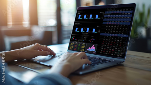 A person is typing on a laptop with a screen displaying graphs and charts