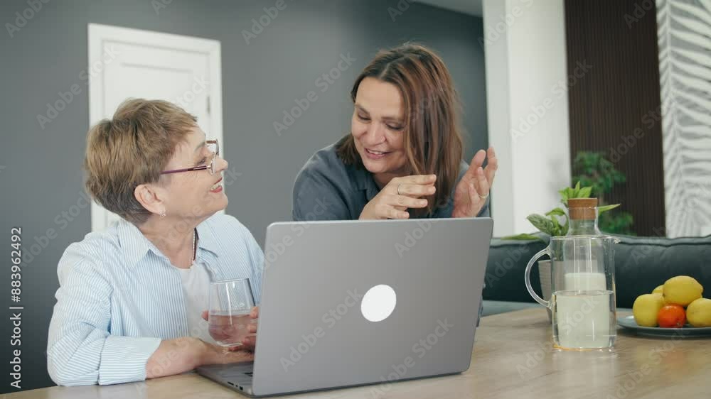 A senior Caucasian woman using a laptop with her adult daughter at home. A senior Caucasian woman using a laptop with her adult daughter at home.
