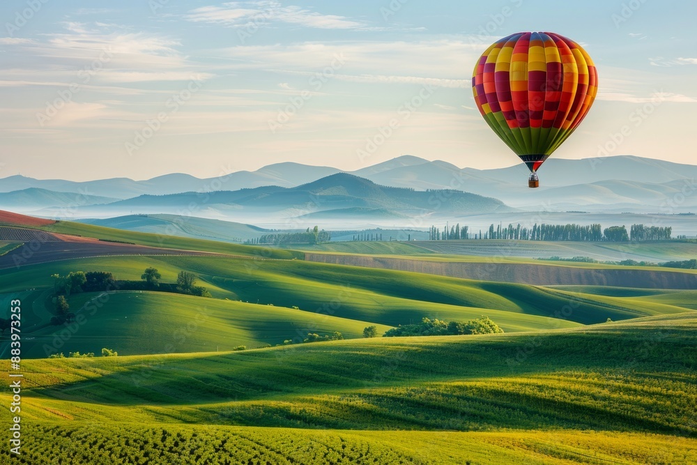 Fototapeta premium A hot air balloon drifting above rolling hills, with a softly blurred background of green fields and distant mountains. 