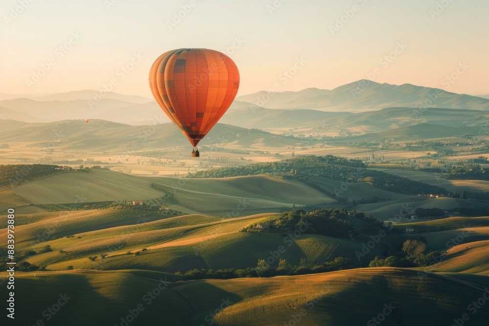 Obraz premium A hot air balloon drifting above rolling hills, with a softly blurred background of green fields and distant mountains. 