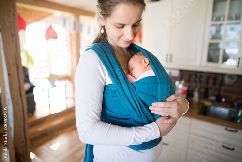 Mother holding small baby, carry her in baby sling, wrap around the house. Unconditional paternal love, mother's Day. © Halfpoint
