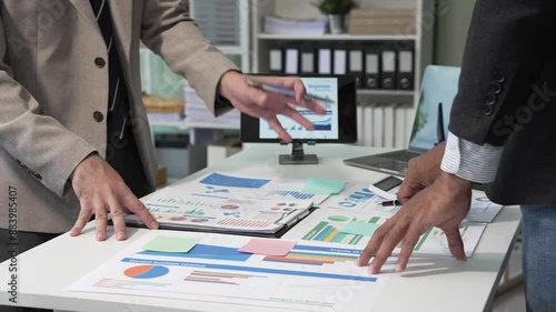 A collaborative meeting at an office desk focusing on teamwork, with discussions centered around financial charts and the sub-account management of work in process in production cost accounting.