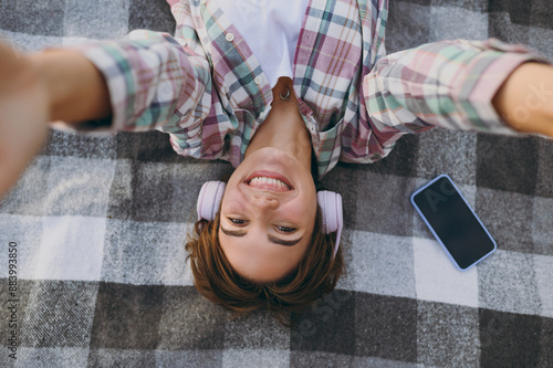 Top view close up young woman wear casual clothes headphones listen music doing selfie shot pov mobile cell phone lay down on plaid rest on sea sand shore in summer day free time. Lifestyle concept. #883993850