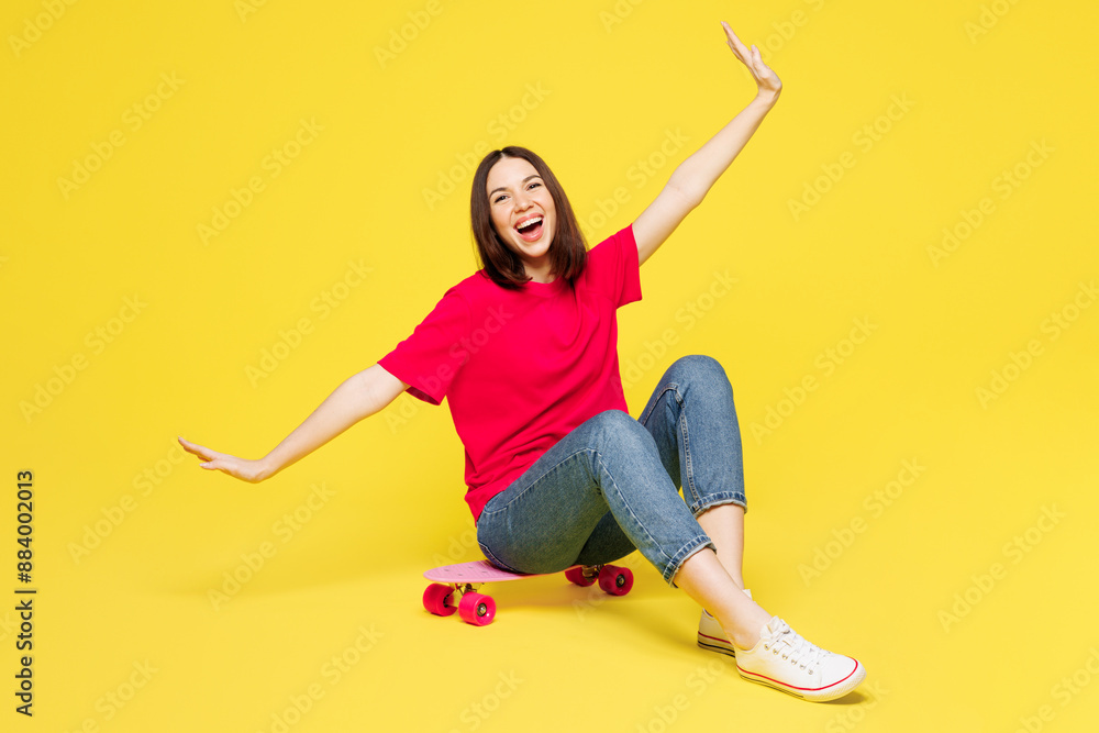 Full body young woman wear pink t-shirt casual clothes sits on skateboard pennyboard with outstretched hands look camera isolated on plain yellow orange background studio portrait. Lifestyle concept. Full body young woman wear pink t-shirt casual clothes sits on skateboard pennyboard with outstretched hands look camera isolated on plain yellow orange background studio portrait. Lifestyle concept.
