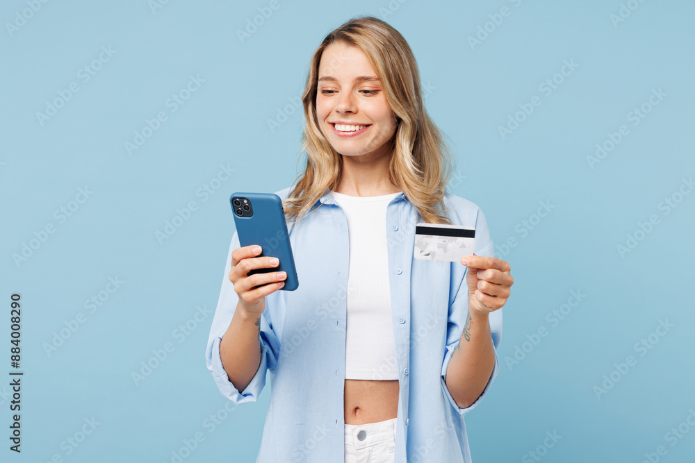 Young woman wears white top shirt casual clothes using mobile cell phone hold credit bank card doing online shopping order delivery booking tour isolated on plain blue background. Lifestyle concept. Young woman wears white top shirt casual clothes using mobile cell phone hold credit bank card doing online shopping order delivery booking tour isolated on plain blue background. Lifestyle concept.