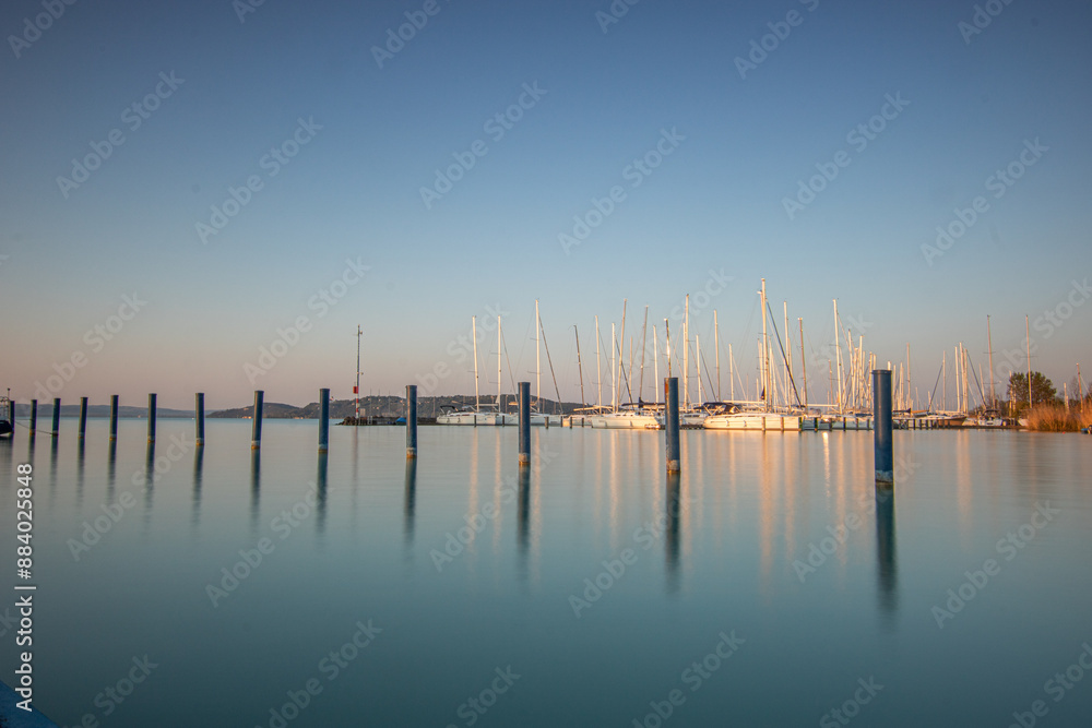 Sunrise on the shore and harbor of a lake in summer. Colorful sky with a wide view of the Horiont. Nature landscape at the marina of Balatonfüred Vitorláskikötő, Balaton, Lake Balaton, Siófok, Hungary Sunrise on the shore and harbor of a lake in summer. Colorful sky with a wide view of the Horiont. Nature landscape at the marina of Balatonfüred Vitorláskikötő, Balaton, Lake Balaton, Siófok, Hungary