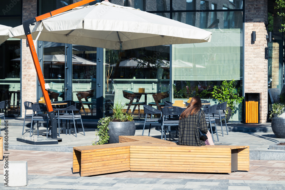 Naklejka premium summer hot temperature restaurant cafe patio furniture space umbrella tables and benches for rest and unrecognizable girl sitting back to camera