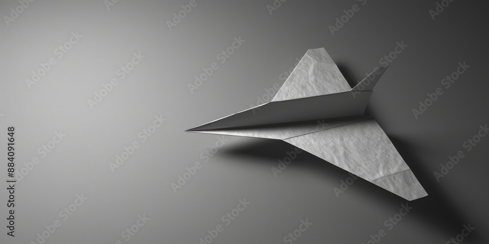 A simple white paper airplane lies on a gray surface, ready to take flight A simple white paper airplane lies on a gray surface, ready to take flight