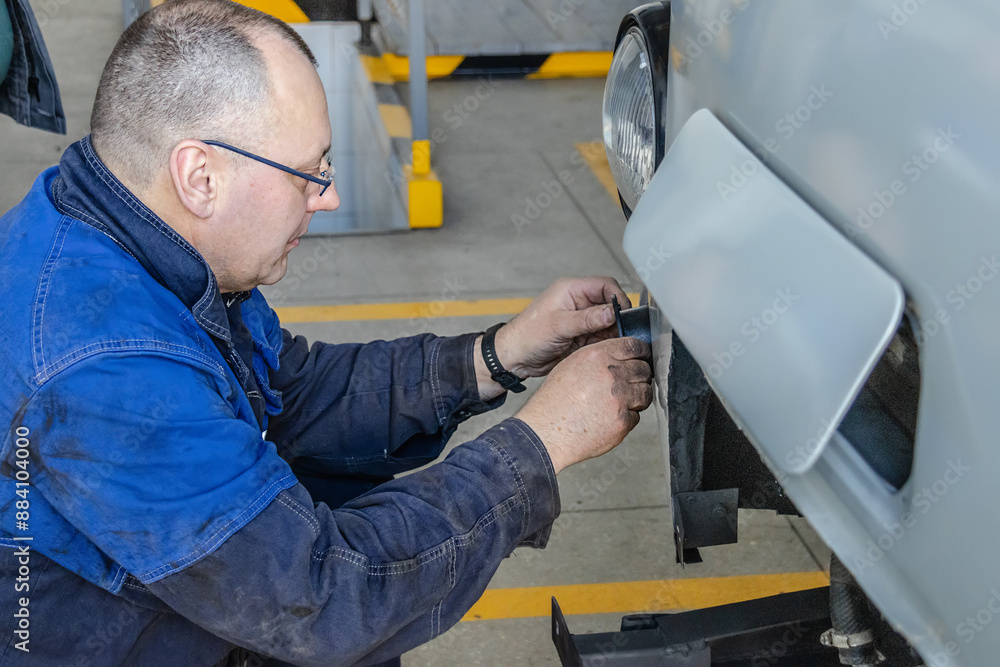A mechanic fixes a car light fixture, working intently on the details of the repair A mechanic fixes a car light fixture, working intently on the details of the repair