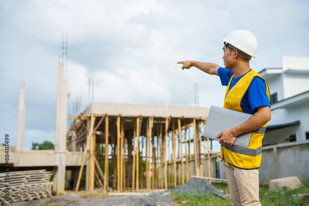 An architect, wearing a hardhat and safety vest, checks a laptop and house plan paper on a clipboard. Blueprints and construction documents lie nearby, emphasizing safety and precision in building. An architect, wearing a hardhat and safety vest, checks a laptop and house plan paper on a clipboard. Blueprints and construction documents lie nearby, emphasizing safety and precision in building.