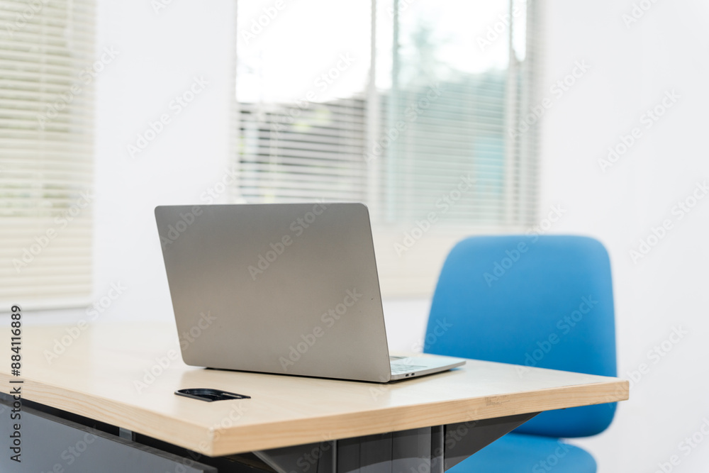 An empty desk in a minimalist office setting, featuring a blank workspace, large windows, a laptop, and a blue office chair against a white wall background, ideal for product montages. no people An empty desk in a minimalist office setting, featuring a blank workspace, large windows, a laptop, and a blue office chair against a white wall background, ideal for product montages. no people