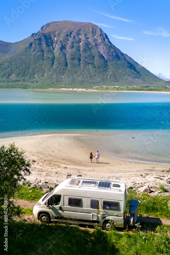 Obraz na plátně A couple walks hand-in-hand on a pristine beach, a campervan parked nearby, with a majestic fjord and mountain backdrop