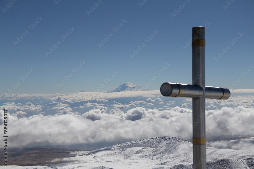 A majestic silver cross stands tall on a snow-capped mountain peak, surrounded by pure white snow and distant mountains under a serene blue sky, evoking awe and tranquility in natures beauty. A majestic silver cross stands tall on a snow-capped mountain peak, surrounded by pure white snow and distant mountains under a serene blue sky, evoking awe and tranquility in natures beauty.