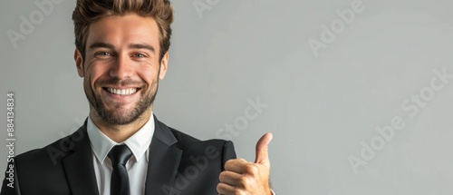  A man in suit and tie, smiling and giving thumbs-up against gray backdrop