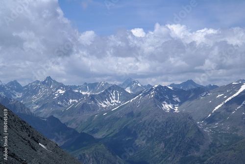 A breathtaking view of a rugged mountain landscape with majestic snow-capped peaks, deep valleys, and a serene blue sky, ideal for outdoor adventure and nature lovers.