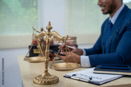 An Asian businessman in a formal suit works alone at a lawyer's desk, by golden scales, law books, leather bags, and a Lady Justice statue, emphasizing personal freedom and legal empowerment. photo