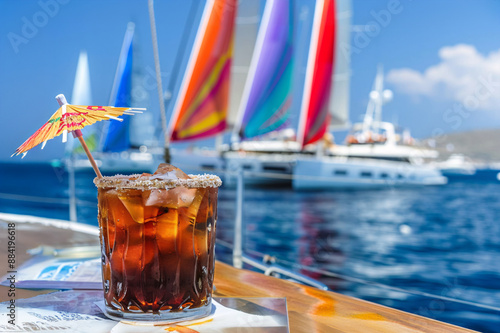 Cocktail with ice and umbrella on the background of the sea. Refreshing drink with ice and straw on the background of yachts. photo