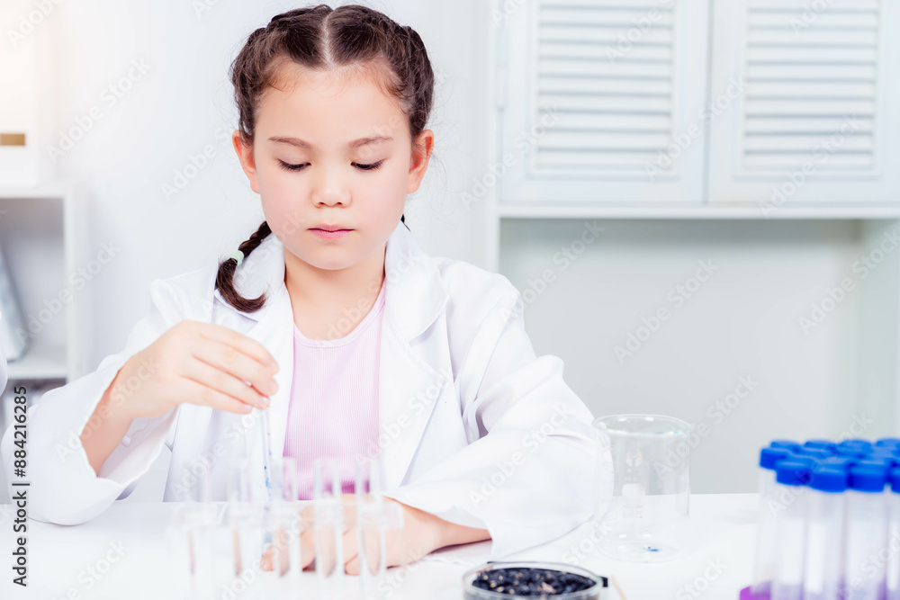 A young girl in a white lab coat conducting experiments with test tubes ...