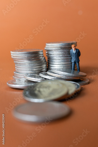 Miniature people A businessman in a suit stands with several stacks of silver coins