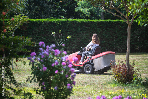 Beautiful young girl enjoying mowing the lawn with a tractor.