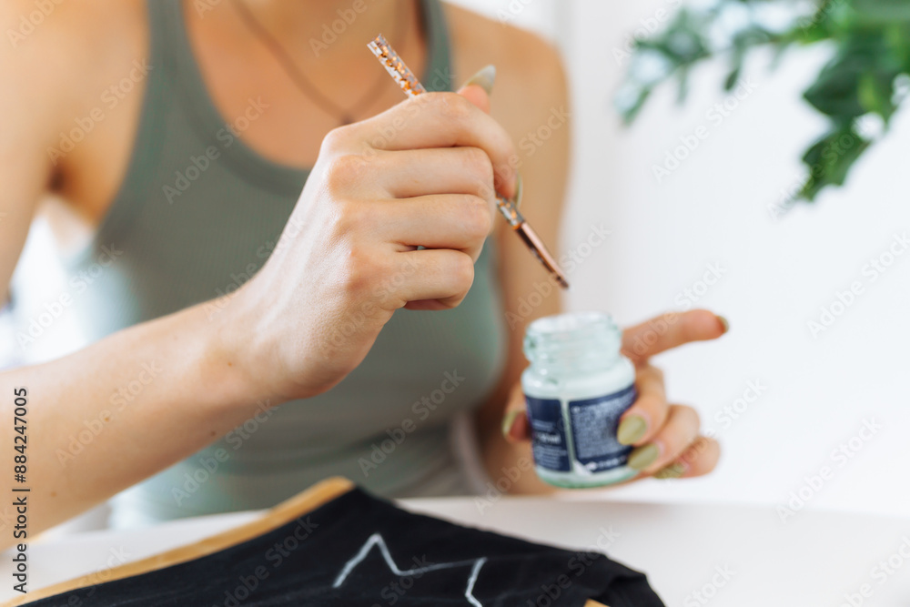 young woman draws picture on clothes with paints, handmade craft work. Customization young woman draws picture on clothes with paints, handmade craft work. Customization