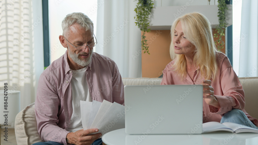 Happy mature modern Caucasian couple elderly senior female woman male man working laptop pc smile. Husband wife businesspeople analyzing documents papers discussing budget e-commerce online sofa home Happy mature modern Caucasian couple elderly senior female woman male man working laptop pc smile. Husband wife businesspeople analyzing documents papers discussing budget e-commerce online sofa home