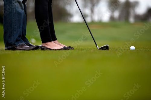 Obraz w ramie Couple standing close on golf course, focusing on putting a golf ball