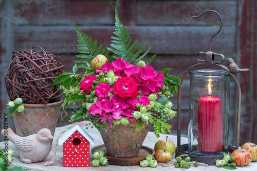 Garten-Arrangement  mit Blumengesteck mit pink Rosen, Hortensienblüten, Haselnüssen, Brombeeren und Blättern im Terracotta-Topf und vintage Laterne photo