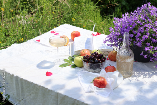 Picnic table with wine, apples, cherry and flowers in the summer garden. Beautiful composition of seasonal fruit and flowers.  photo