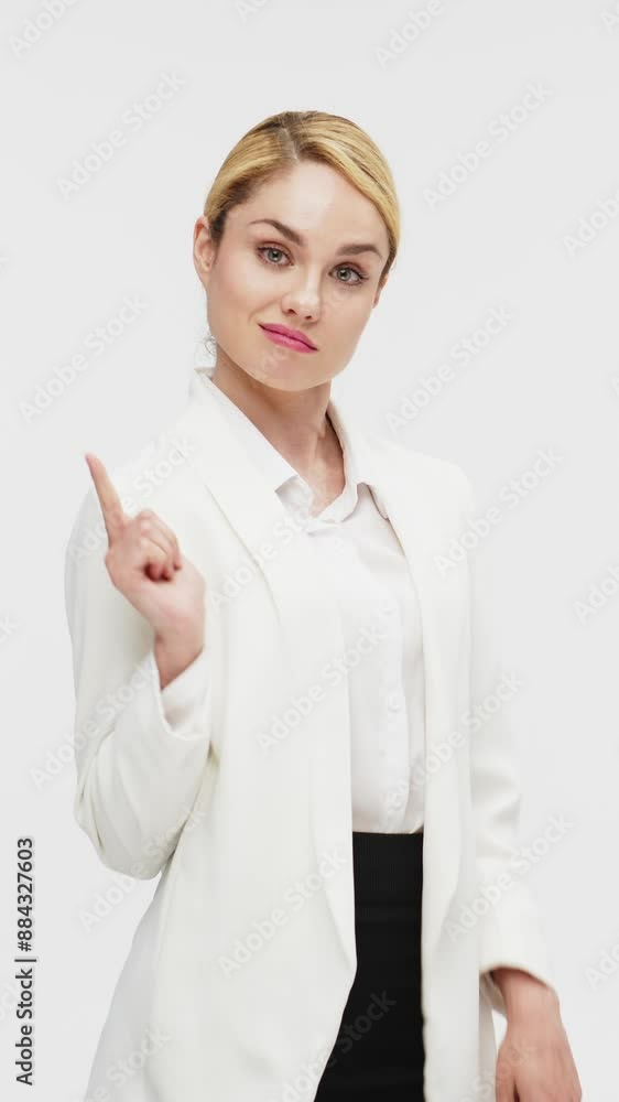 Vertical video. A business blonde woman in a stylish business suit on a white background confidently points her finger at the bottom of the screen. Business, business decisions and finance concept. Vertical video. A business blonde woman in a stylish business suit on a white background confidently points her finger at the bottom of the screen. Business, business decisions and finance concept.