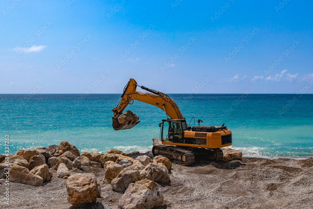 An excavator is working on the oceanfront, placing rocks for coastal construction