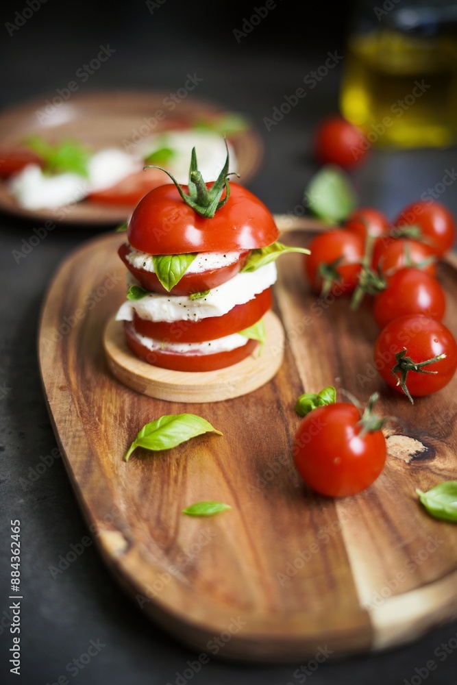 Stacked caprese salad with tomato, mozzarella cheese, and basil leaves on wooden board Stacked caprese salad with tomato, mozzarella cheese, and basil leaves on wooden board