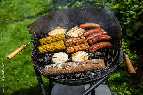 Ein Holzkohlegrill mit Würstchen Maiskolben Baguette,  und Grillkäse belegt. photo