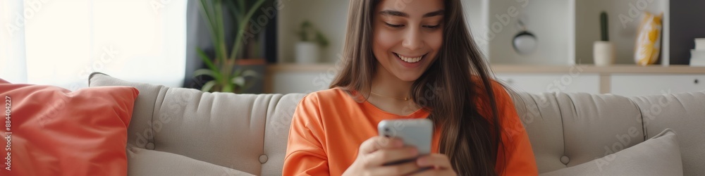 A woman relaxes at home, smiling and texting on her smartphone, enjoying the moment. A woman relaxes at home, smiling and texting on her smartphone, enjoying the moment.