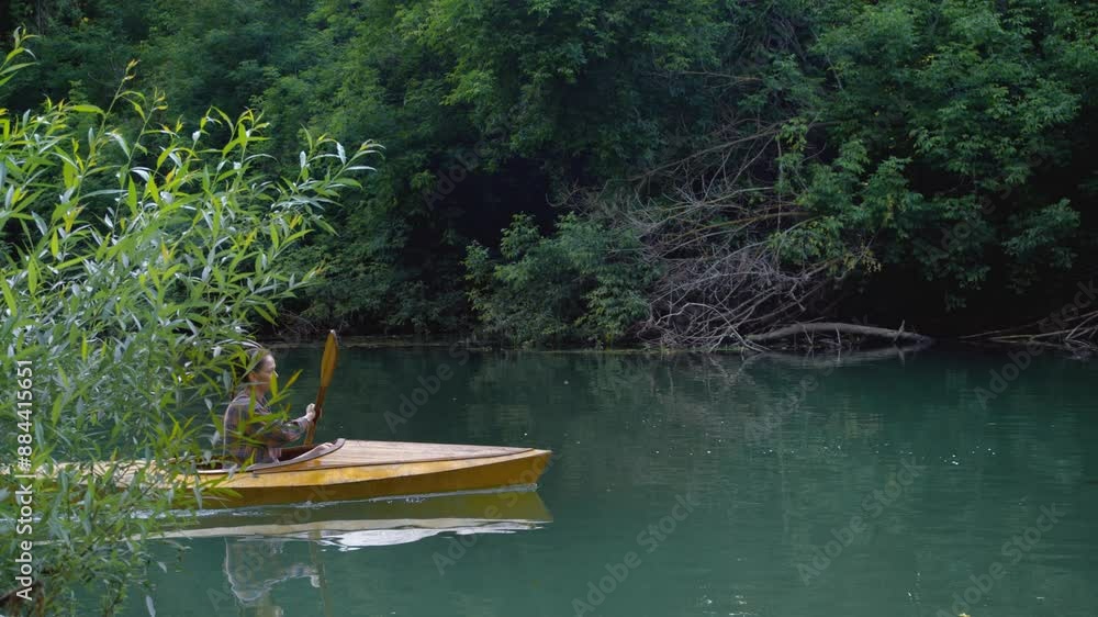 A young and beautiful woman gracefully glides on a wooden kayak, expertly navigating a beautiful river using oars. A young and beautiful woman gracefully glides on a wooden kayak, expertly navigating a beautiful river using oars.