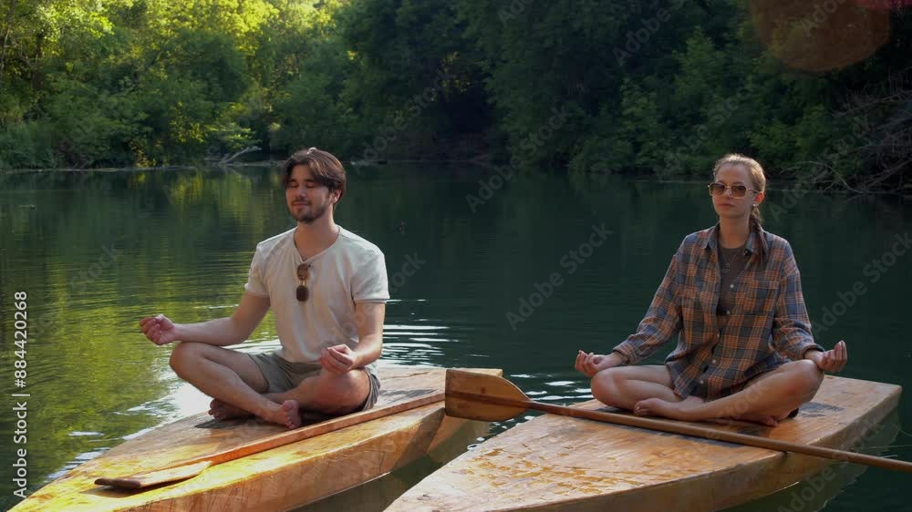 Young couple are engaged in meditation, sitting on rafts in the river. The man is learning from his teacher how to meditate. Young couple are engaged in meditation, sitting on rafts in the river. The man is learning from his teacher how to meditate.