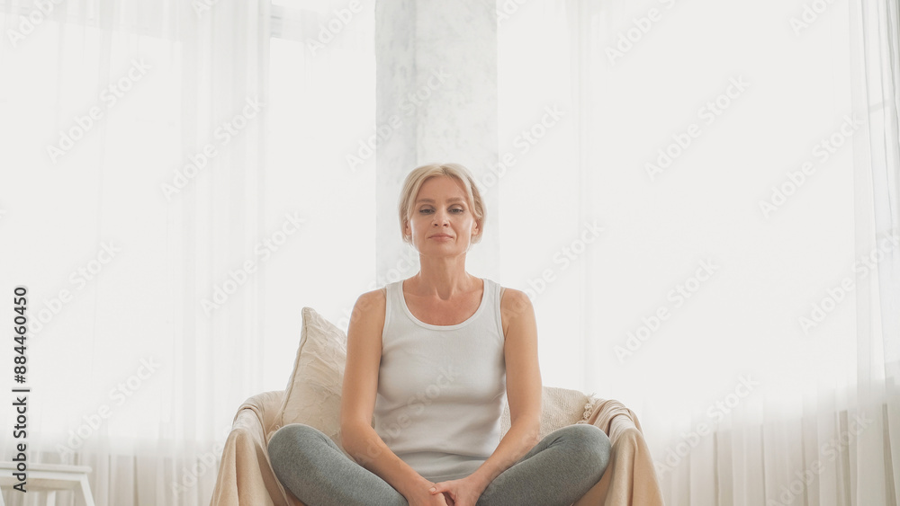 Relaxation practice. Peaceful morning. Home meditation. Harmony smiling woman sitting in lotus pose on couch breathing in light interior copy space. Relaxation practice. Peaceful morning. Home meditation. Harmony smiling woman sitting in lotus pose on couch breathing in light interior copy space.